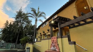 A yellow building with a pergola, a statue, and a parking lot. - The Aqua Pacific Hotel (Santa Cruz)