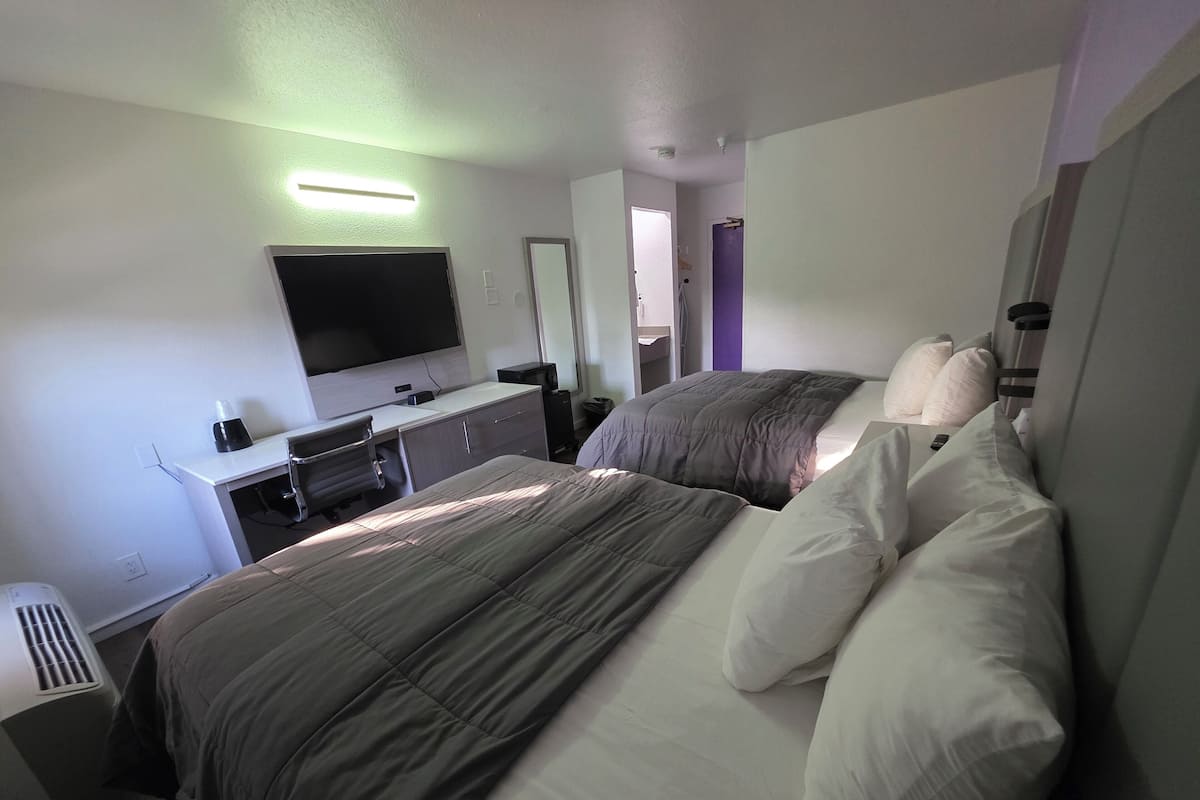 Une chambre d’hôtel avec deux lits, un bureau doté d’un téléviseur à écran plat, une commode et une salle de bain visible à travers une porte ouverte.