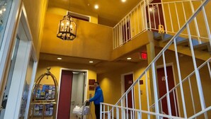 A hotel lobby with a yellow color scheme, a double staircase, and a person pushing a luggage cart. - The Aqua Pacific Hotel (Santa Cruz)