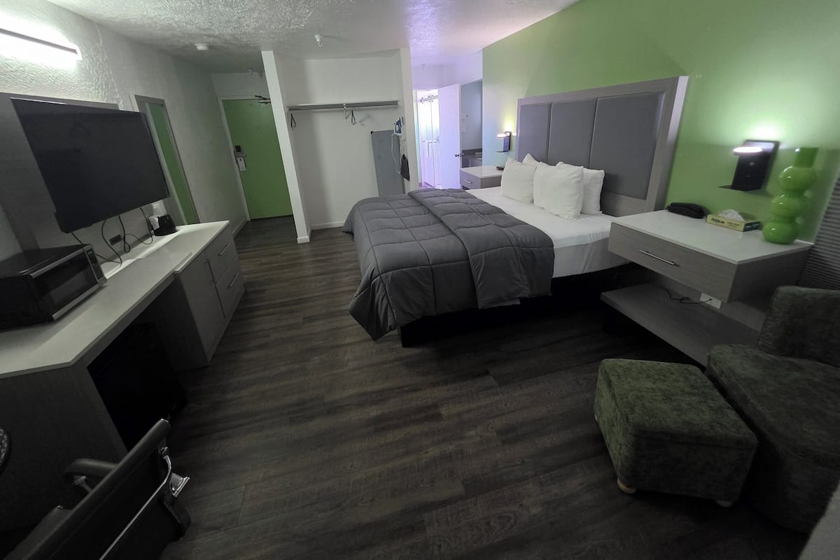 Une chambre d’hôtel avec un lit, un bureau avec un ordinateur, une télévision et un mur vert.