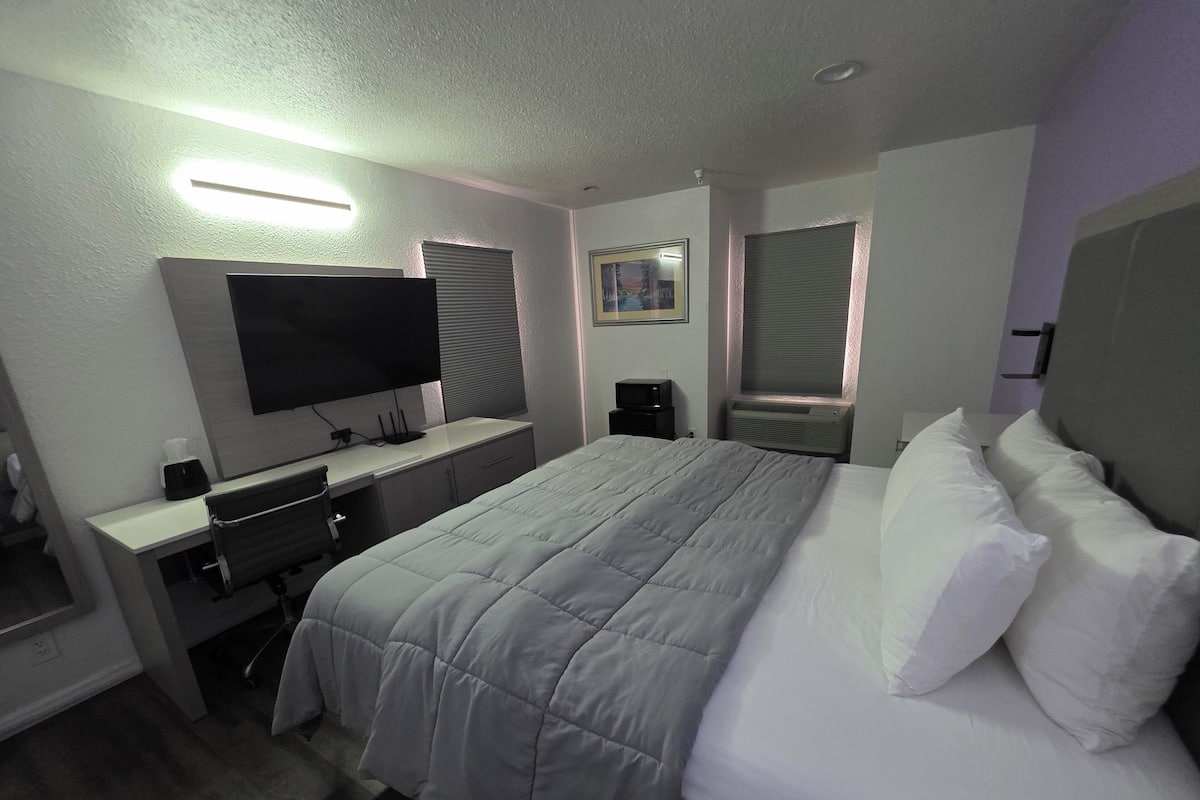 Une chambre d’hôtel moderne dotée d’un grand lit, d’un bureau avec un téléviseur à écran plat, d’un miroir et d’une fenêtre avec des stores.