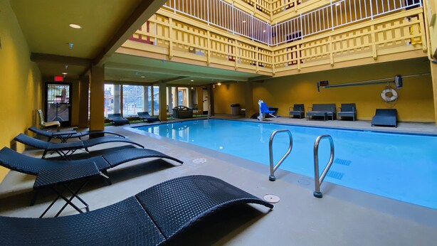An indoor swimming pool with lounge chairs and a high ceiling with a balcony. - The Aqua Pacific Hotel (Santa Cruz)
