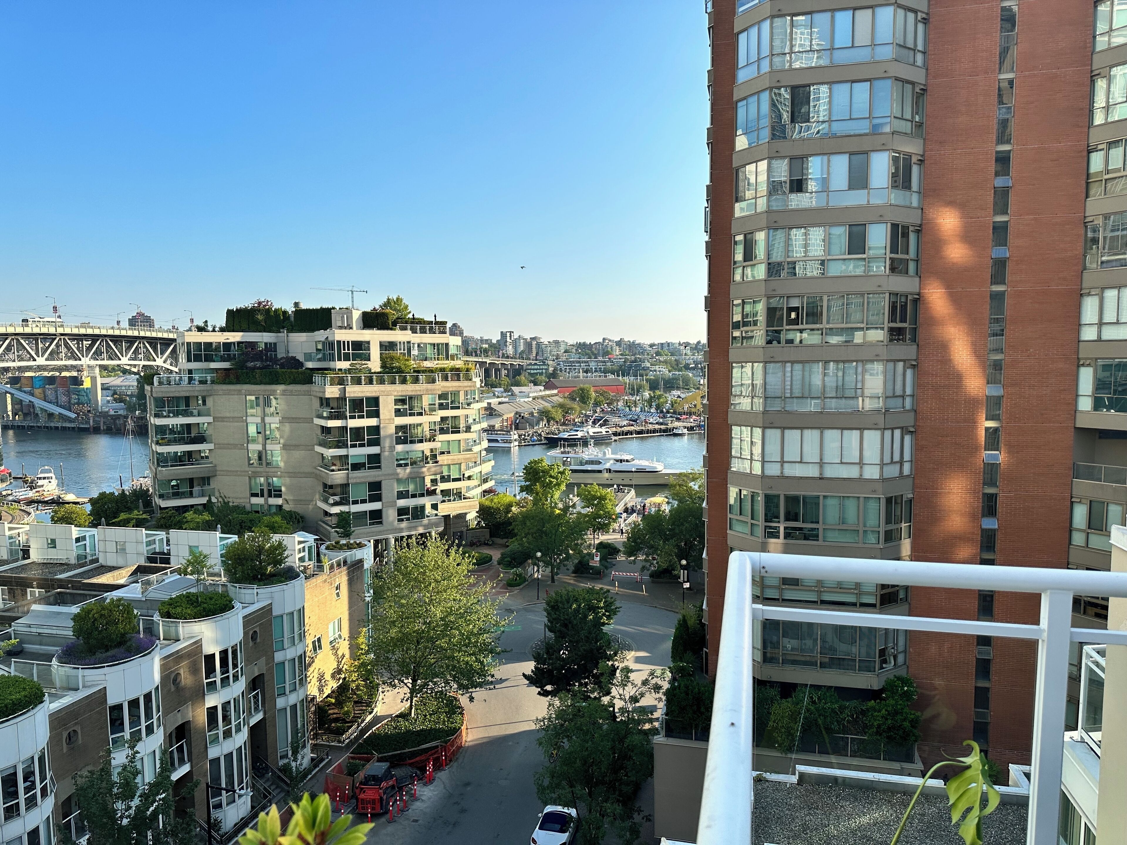 A high-rise building with multiple balconies overlooking a marina with boats and a bridge in the background.
