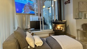 A cozy living room with a large flat-screen TV, a fireplace, and a sofa with cushions.