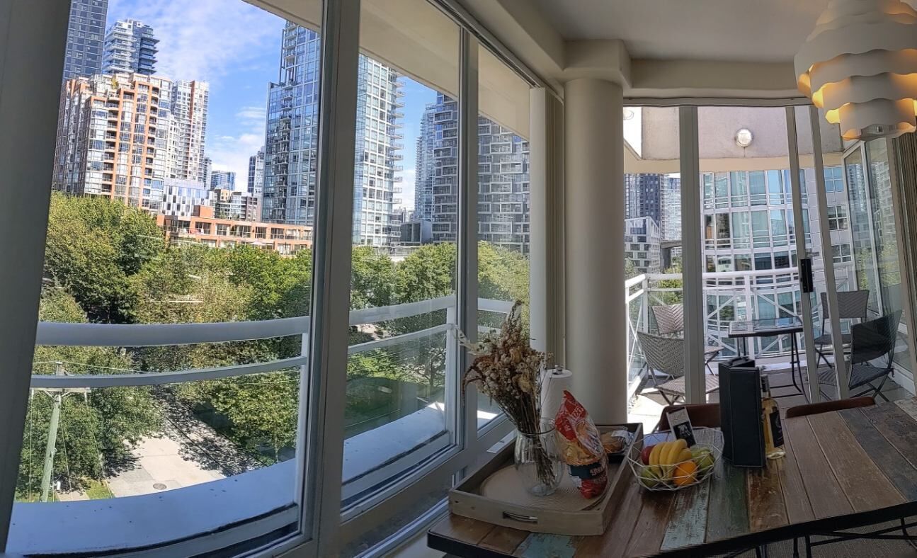 Eine moderne Wohnung mit großen Fenstern und Blick auf die Stadt, inklusive Balkon mit Gartenmöbeln sowie Essbereich mit Tisch und Stühlen.