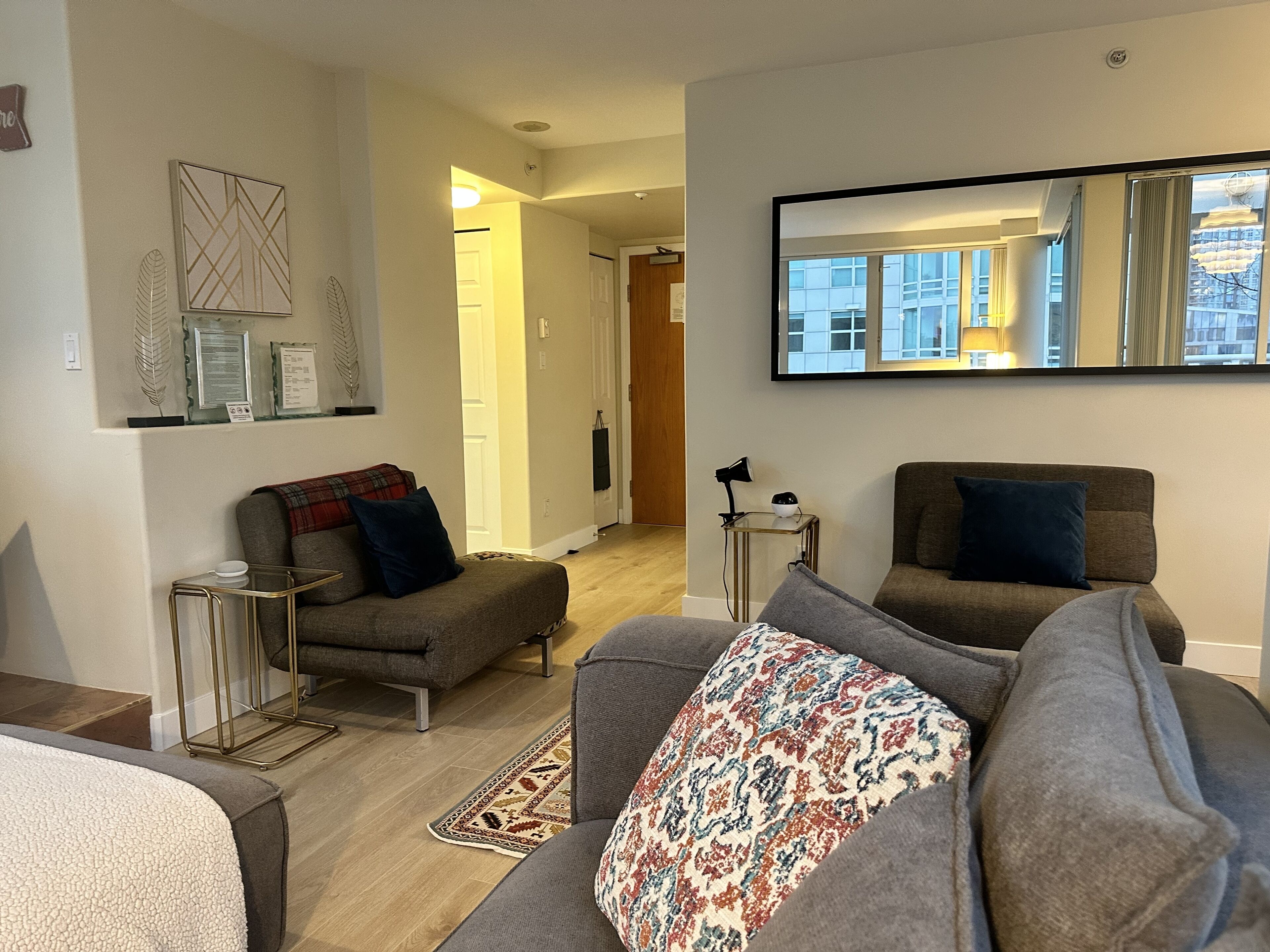 A modern living room with a grey sofa, a patterned throw, and a small side table with a lamp.