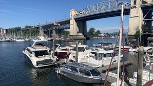 A marina with various boats docked, a bridge in the background, and a clear sky.