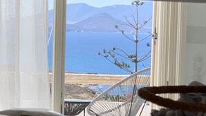 Une pièce avec vue sur la mer et les montagnes. On y trouve une chaise blanche et une petite table sur laquelle est posé un panier.