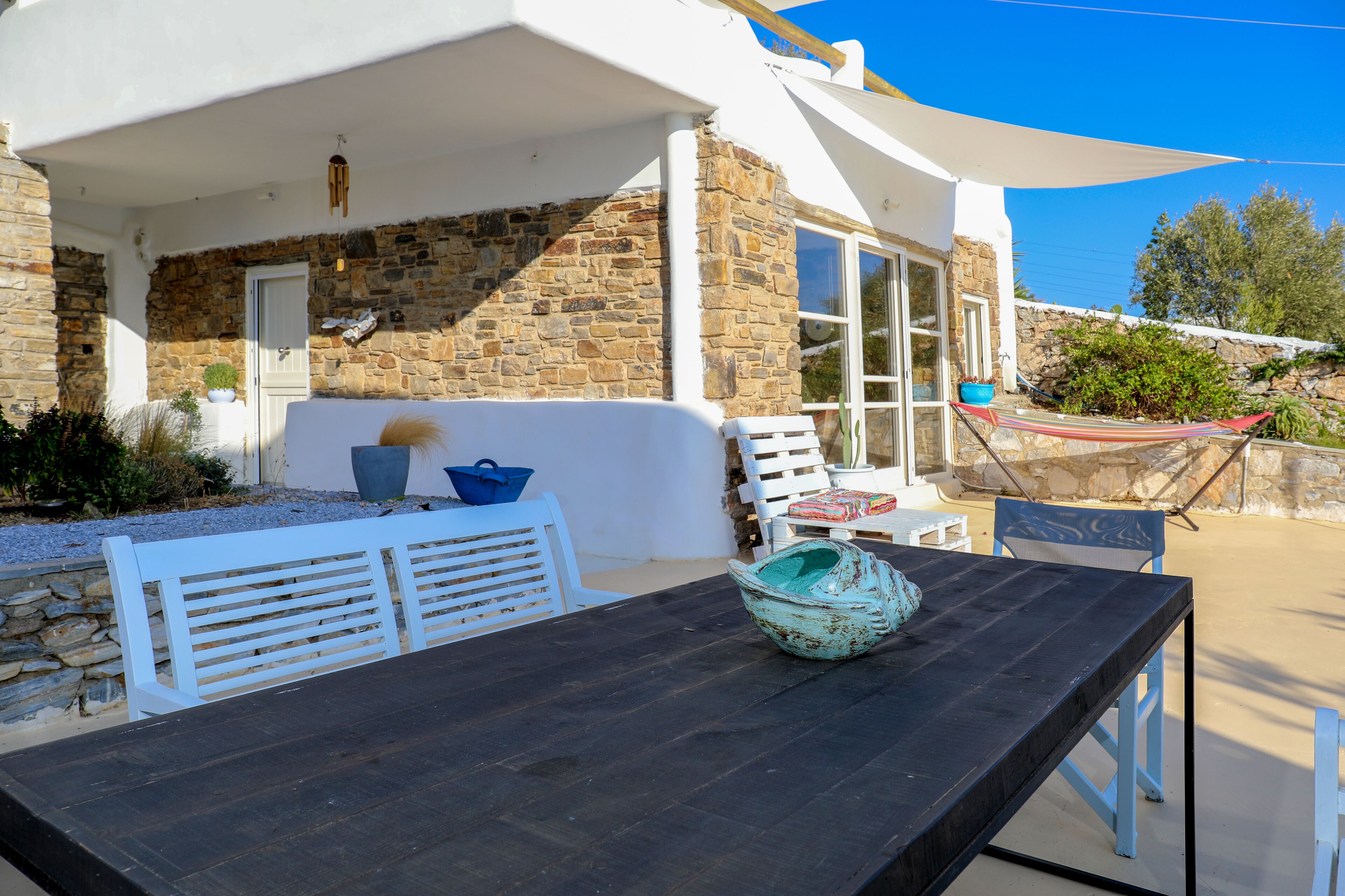 An outdoor seating area with a wooden table, white chairs, and a blue bowl.