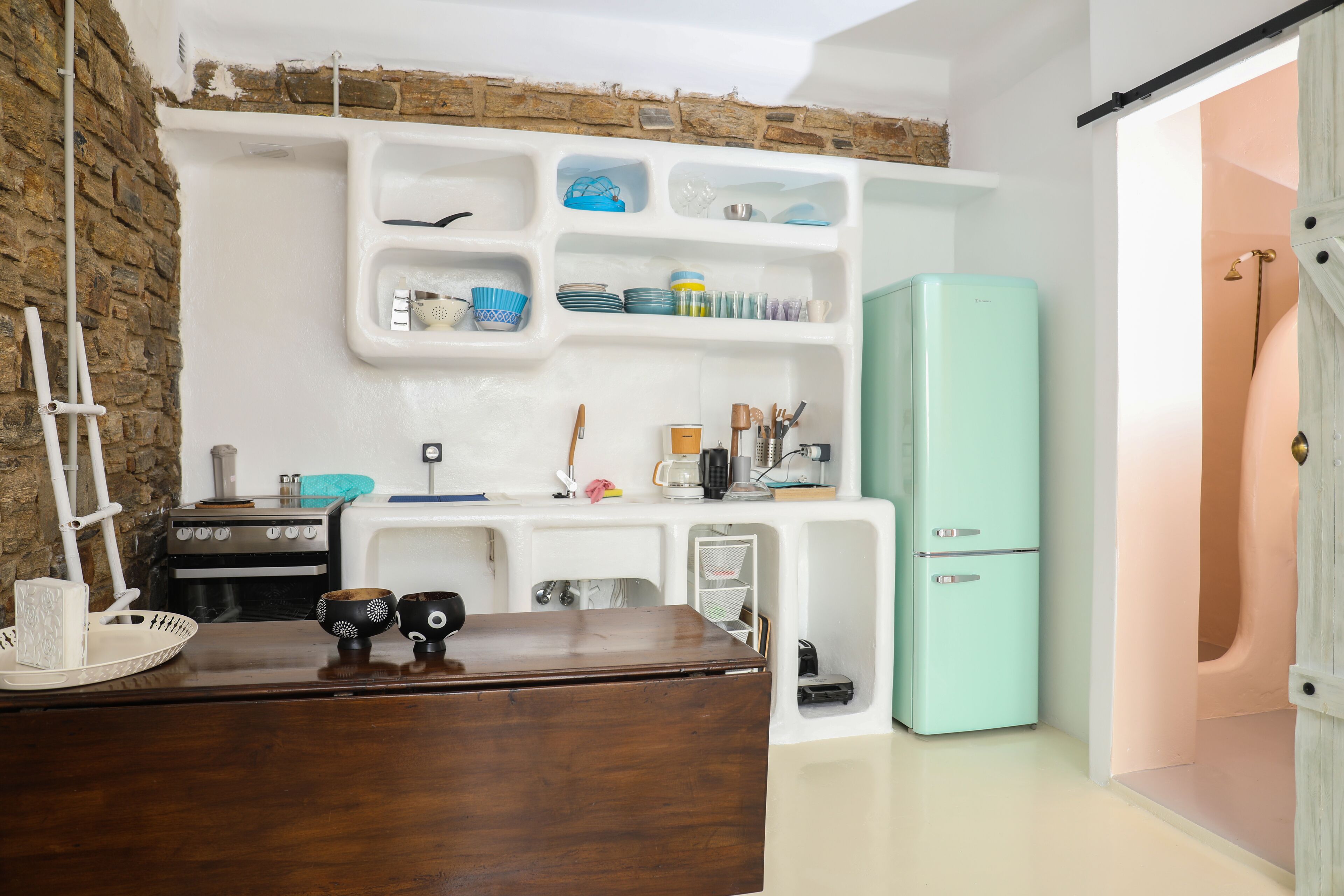 A compact kitchen with white cabinetry, a teal refrigerator, and a wooden countertop.