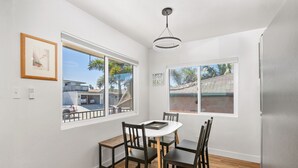 A dining area with a round table, four chairs, and two windows offering views of a residential area. - Renovated 2 BD! Walk to Beach, Restaurants, Bars! (San Diego)