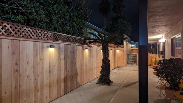 A wooden fence with lights, a palm tree, and a concrete pathway leading to a building. - Renovated 2 BD! Walk to Beach, Restaurants, Bars! (San Diego)