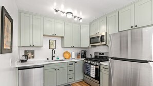 A modern kitchen with light green cabinets, stainless steel appliances, and a wooden floor. - Renovated 2 BD! Walk to Beach, Restaurants, Bars! (San Diego)