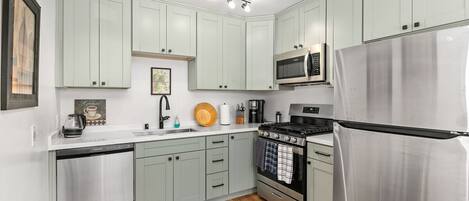 Una cocina moderna con armarios verde claro, electrodomésticos de acero inoxidable y suelo de madera.