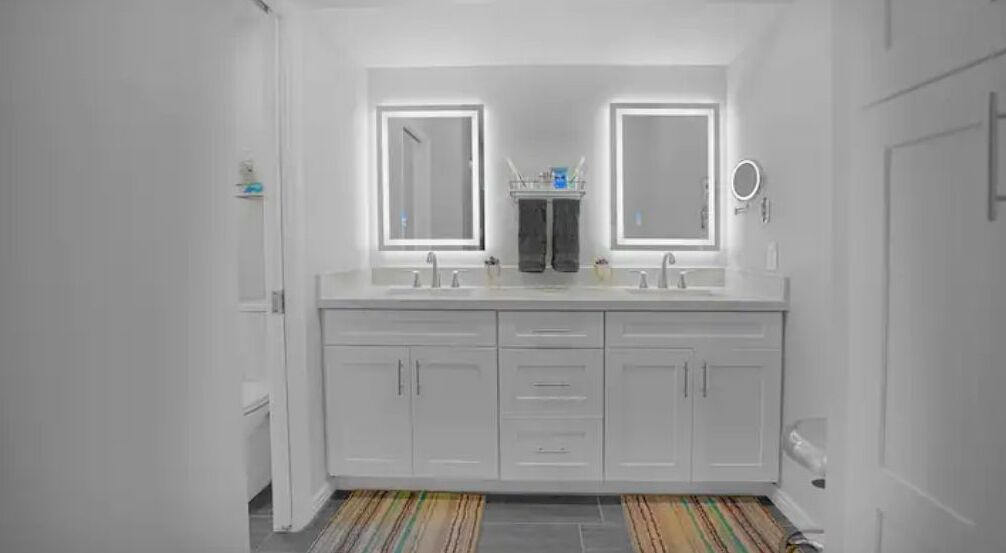 Een moderne badkamer met een wit wastafelmeubel, twee spiegels en een gestreepte vloer.