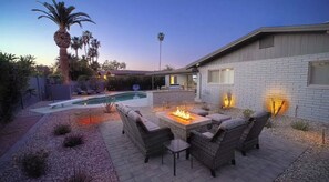 A backyard with a pool, outdoor seating, and a fire pit.