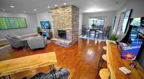 A modern living room with a stone fireplace, wooden flooring, a grey sofa, a wooden coffee table, and a TV.