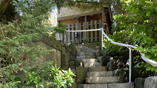 Una escalera de piedra que sube hacia una estructura de madera, rodeada de vegetación.