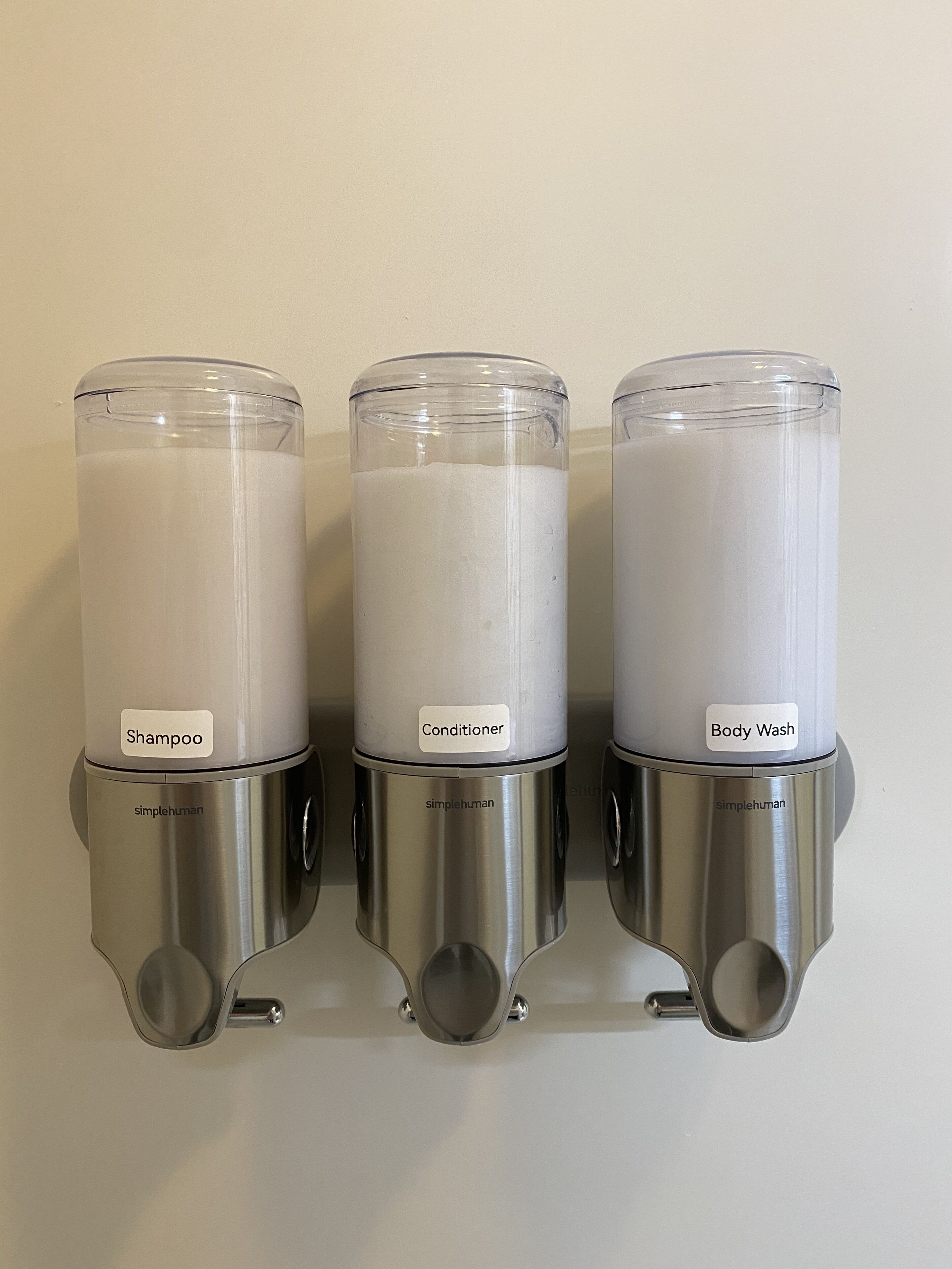 Three wall-mounted dispensers labeled with different hair care products: shampoo, conditioner, and body wash.