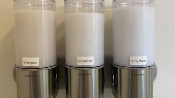 Three wall-mounted dispensers labeled with different hair care products: shampoo, conditioner, and body wash.