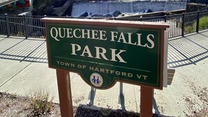 A sign for Quechee Falls Park with a waterfall in the background.