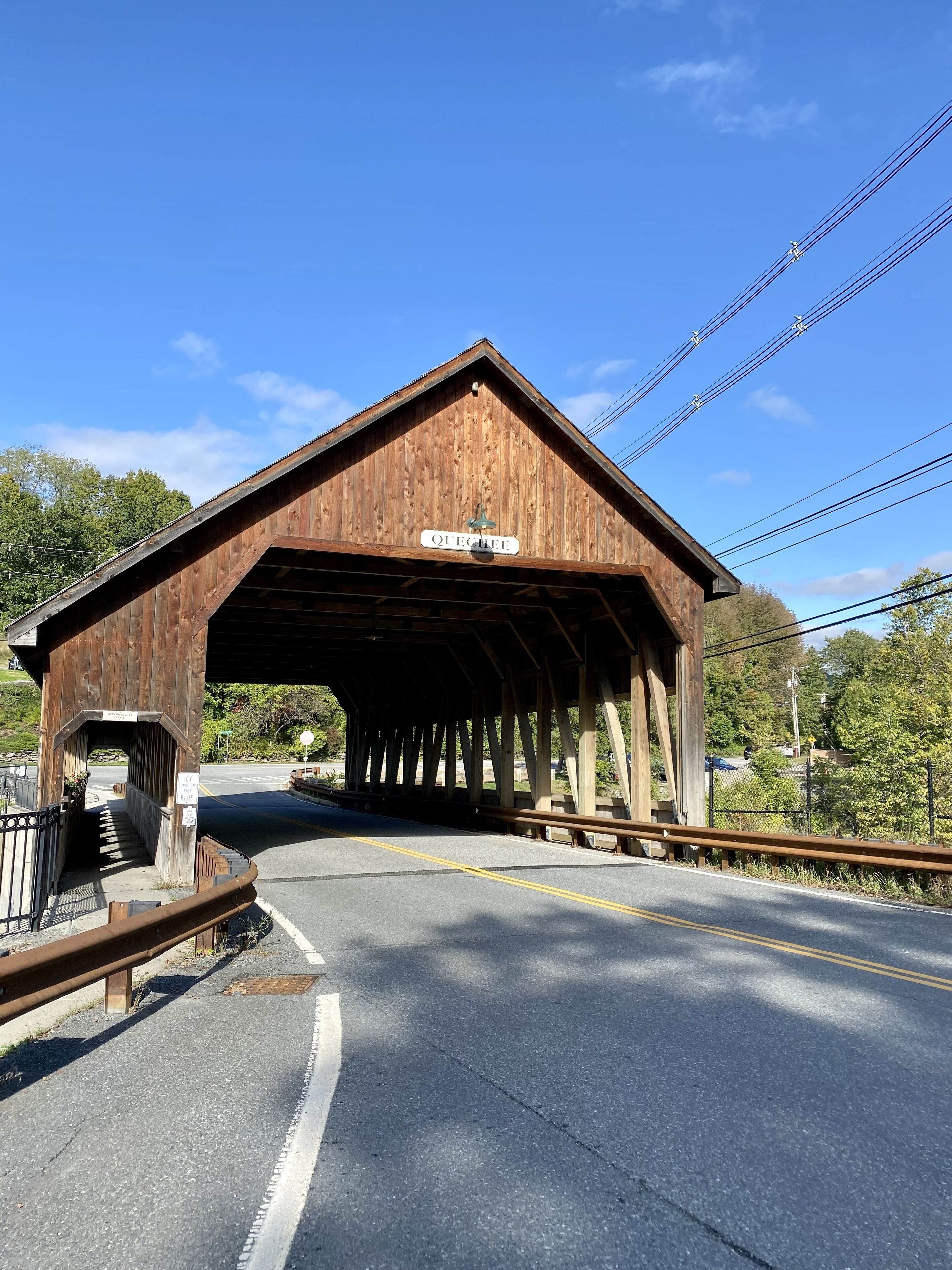 A wooden covered bridge with a sign reading 'QUECHUA' and a road passing underneath.