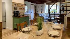A dining area with a wooden table set for four, a green kitchen island, and a staircase leading to a lofted living area.
