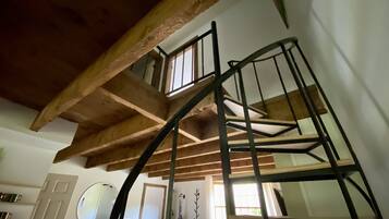 A spiral staircase with wooden beams and metal railings in a room with a white door, a round mirror, and a window.