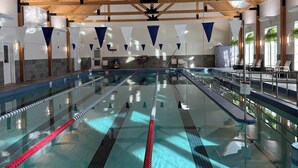 An indoor swimming pool with multiple lanes, wooden beams, and a tiled floor.