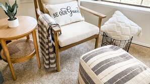 Una habitación acogedora con una silla de madera, una mesita redonda con una planta y un ventanal con vista a la vegetación.