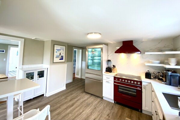 A modern kitchen with white cabinetry, a red stove, and a glass-fronted refrigerator. - Exquisite Oceanfont Cottage at Madaket Beach! (Nantucket)