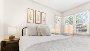 Un dormitorio con una cama grande, una mesita de noche con una lámpara y cuadros con hojas en la pared.