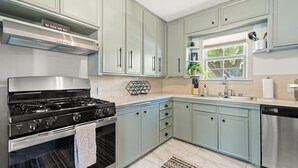 Una cocina con armarios azul claro, electrodomésticos de acero inoxidable y un ventanal con vistas al verdor.