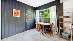Un área de comedor con una pared de madera oscura, un cuadro enmarcado, una ventana con cortinas y una estantería de bambú.