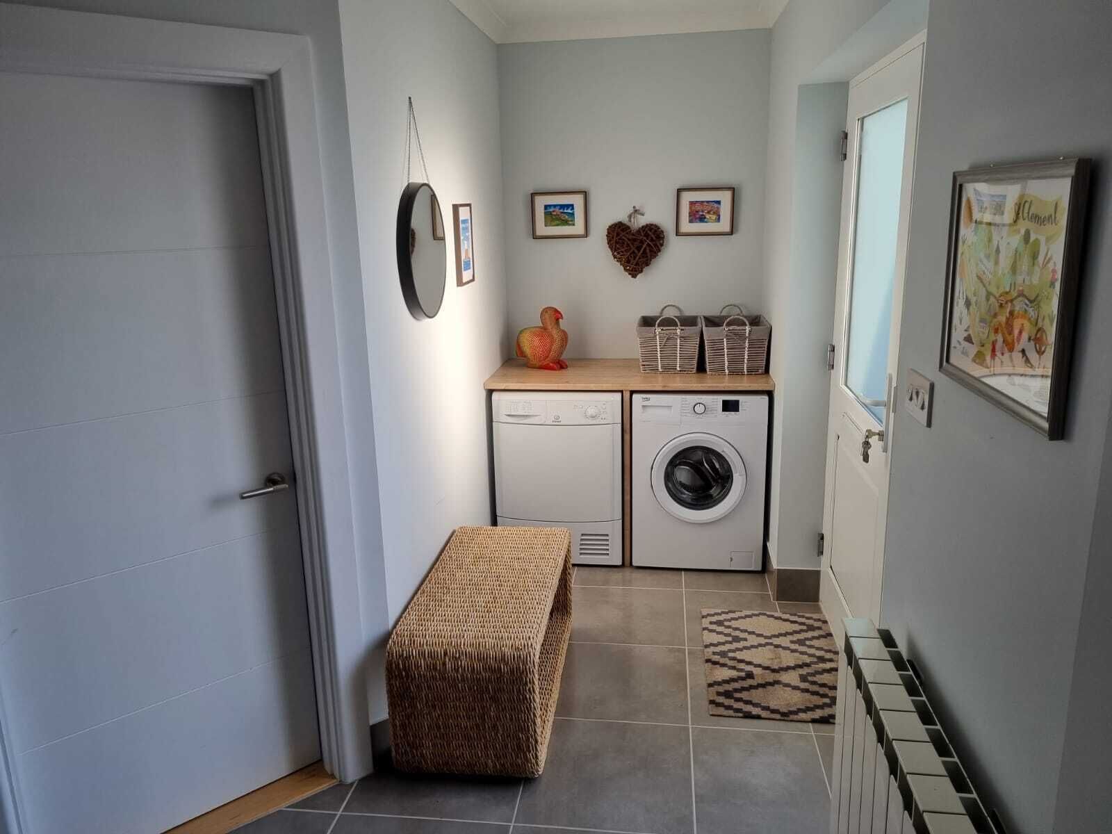 A laundry room with a washing machine, a dryer, and a bench. There are framed pictures on the wall and a basket on the counter.