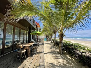 Una terraza de madera con asientos al aire libre, un parasol verde y vista a la playa.