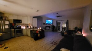 A modern kitchen with a central island, a dining area with a dark-colored sofa, and a living room with a television.