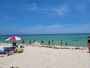 Une plage où des gens se prélassent au soleil et se baignent. On y trouve des chaises de plage et des parasols.