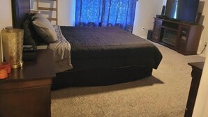 A bedroom with a bed, a dresser, a television, and a window with curtains.