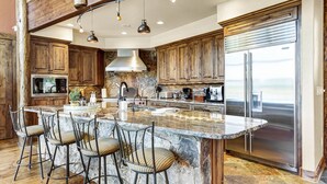 Un'ampia cucina con un'isola grande, mobili in legno, un frigorifero in acciaio inossidabile e una parete di fondo in pietra.