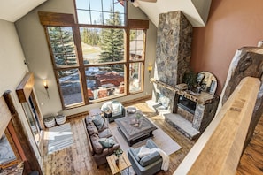A spacious living area with a stone fireplace, large windows offering a view of a snowy landscape, and a cozy seating arrangement.