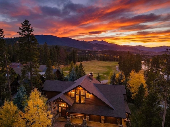 A lodge with a large window, surrounded by trees and a view of a mountain range.