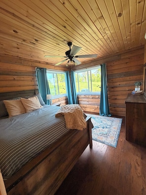 Un dormitorio de cabaña de madera con cama, ventilador de techo y vistas al exterior.