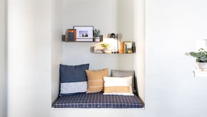 Un coin douillet avec un banc rembourré, une petite étagère avec des livres et des objets décoratifs, et une plante en pot.