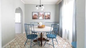 Un coin repas avec une table ronde, des chaises bleues et un lustre. Trois tableaux encadrés ornent le mur.