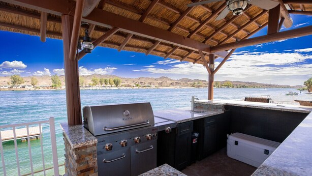 Cocina al aire libre con parrilla, pileta y encimera, con vista a un cuerpo de agua bajo un cielo despejado.