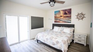 Un dormitorio con cama, ventilador de techo, ventana, una obra de arte en la pared y un adorno con timón de barco.