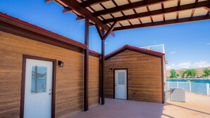 Un espacio al aire libre techado con dos puertas de madera, techo metálico y vista a un cuerpo de agua y montañas al fondo.