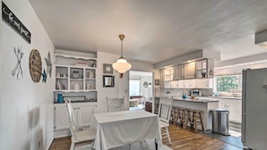 A modern kitchen with white cabinetry, a dining area with a white table and chairs, and a hanging light fixture. - Near Snoqualmie River! Cozy Home in Rural Setting (Carnation)