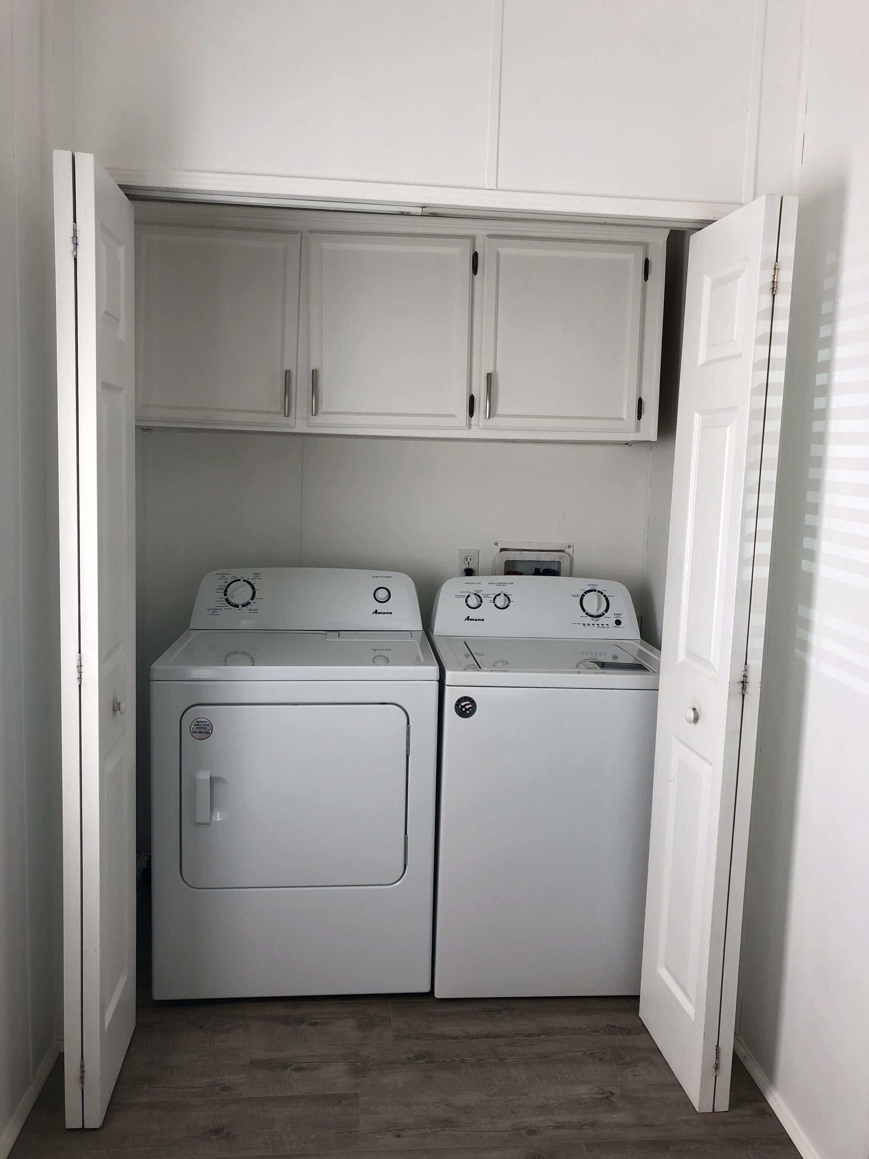 A laundry room with two white washing machines and a cabinet above them.